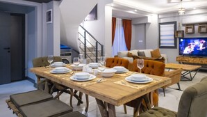 Una sala moderna con una mesa de comedor de madera dispuesta para cuatro personas, un sofá, un televisor y una escalera.