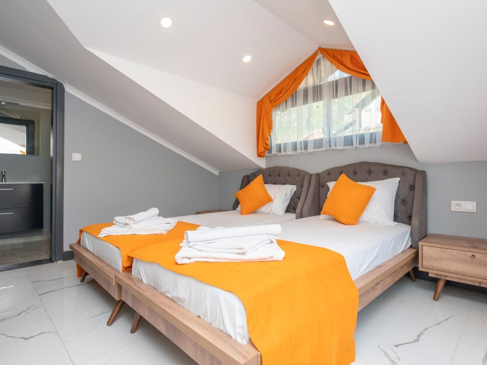A modern bedroom with a large bed, two pillows, a nightstand, and a window with curtains.