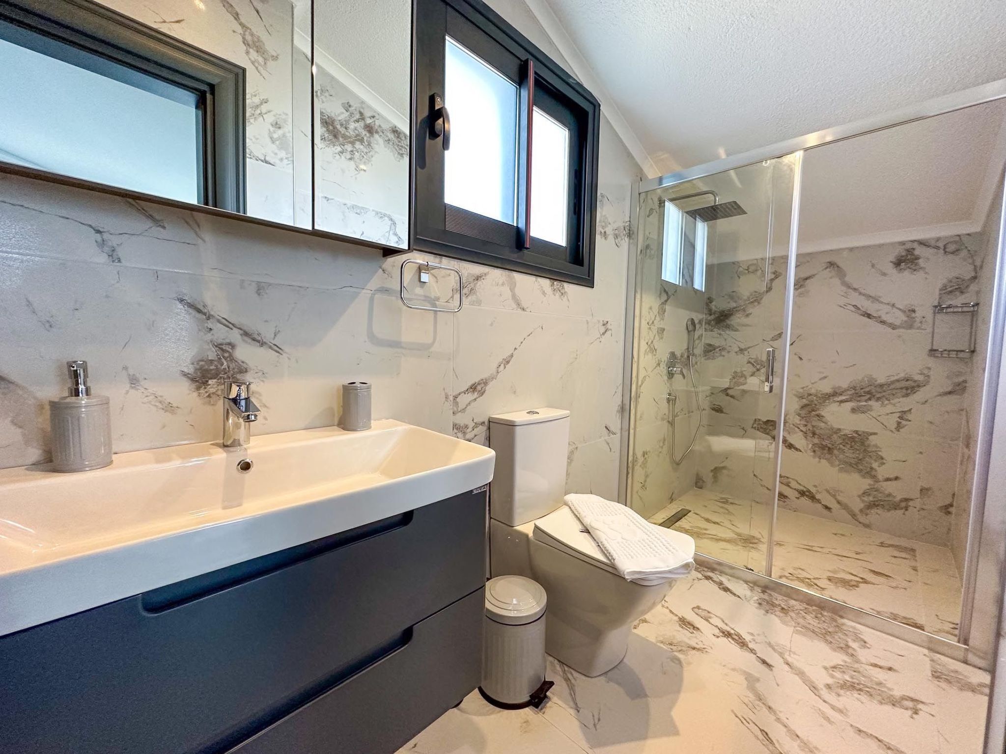 A bathroom with a marble sink, a glass shower enclosure, and a toilet.