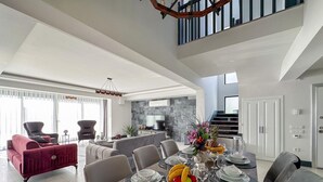 Ein geräumiger Essbereich mit hoher Decke, modernen Möbeln und Blick auf die Küche und das Wohnzimmer.