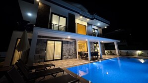 Ein modernes, zweistöckiges Haus mit Swimmingpool, Außenbereich zum Sitzen und einer überdachten Terrasse.