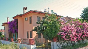 Une maison à deux étages, avec un toit recouvert de tuiles rouges, une façade de couleur beige et une allée gravillonnée.