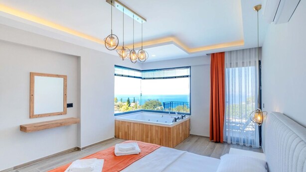 A modern hotel room with a large bed, a view of the sea, a jacuzzi, and a wooden shelf. - Villa mit Infinitypool in Fethiye Faralya by Interhome (Ölüdeniz)