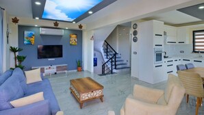 A modern living room with a flat-screen TV, a sofa, a coffee table, and a dining area with chairs.