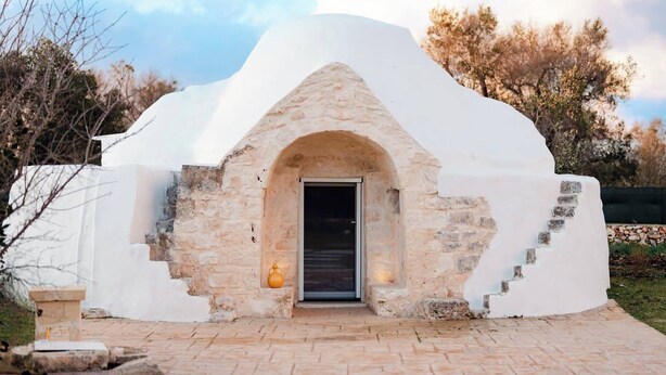 Un edificio blanco de forma abovedada con un arco de piedra, un pequeño aplique exterior y un sendero de ladrillo que conduce a él.