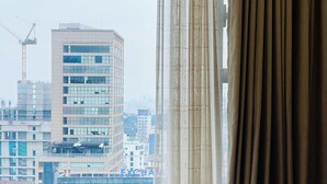 Una camera d'albergo con un letto, una finestra con tende e vista su un panorama urbano con edifici e una gru.