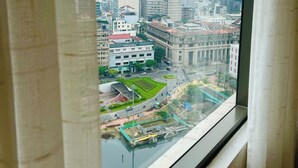 Paesaggio urbano visibile da una finestra, con un edificio moderno, una banca e una zona verde con un ponte.