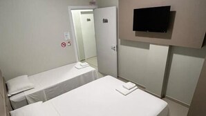 A small, clean room with two single beds, a flat-screen TV mounted on the wall, and a door leading to another room. - Hotel Catarina (Sao Miguel Do Oeste)