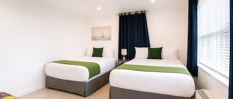 A hotel room with two beds, a small table, and a window with curtains.