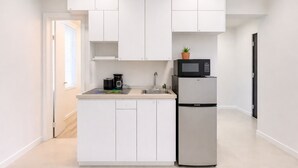 Eine moderne Küche mit weißen Schränken, einem Edelstahl-Kühlschrank, einer Mikrowelle und einer Kaffeemaschine.