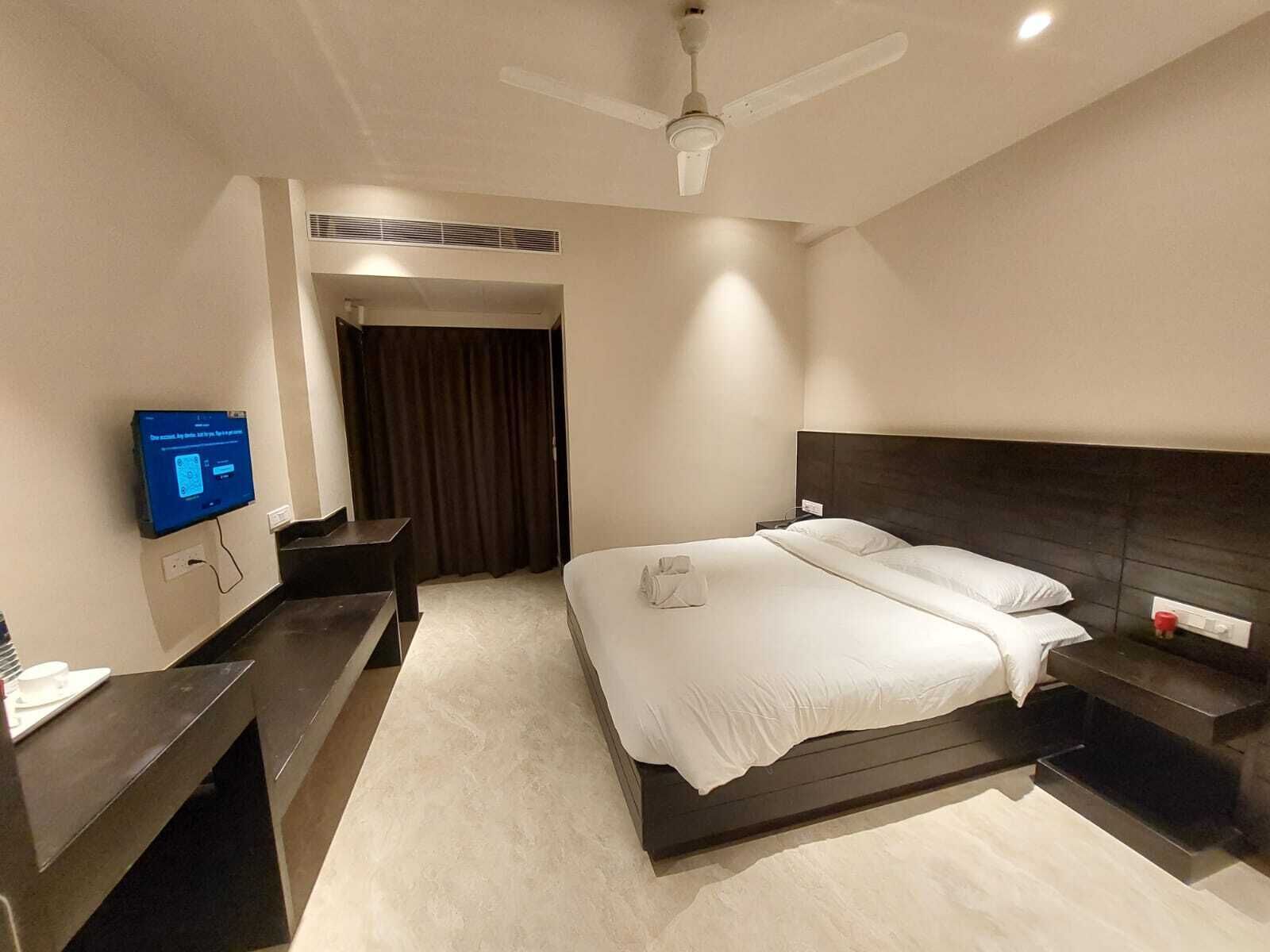 A modern hotel room with a large bed, bedside tables, a TV, and a ceiling fan.