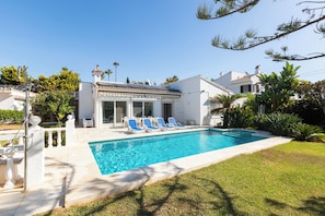 A swimming pool with lounge chairs, a white building with columns, and surrounding greenery. - Villa Marbesa Beach (Marbella)
