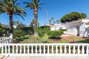 A white building with a tiled roof, surrounded by a well-maintained garden with palm trees and a white fence. - Villa Marbesa Beach (Marbella)