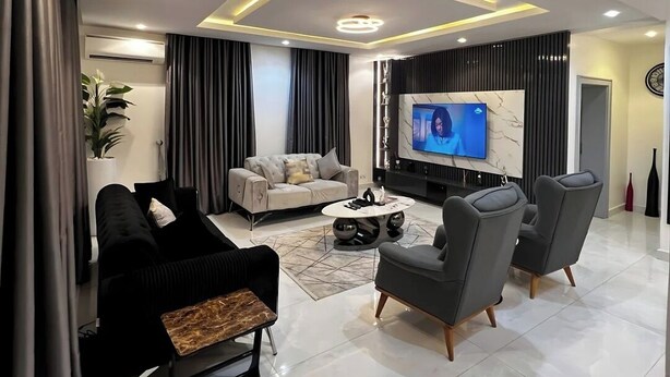 A modern living room with a sofa, armchairs, a coffee table, and a TV. - JOEY HOMES  (Abuja)