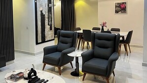 A modern living room with a round coffee table, two black armchairs, a white dining table with chairs, and a ceiling light fixture. - JOEY HOMES  (Abuja)
