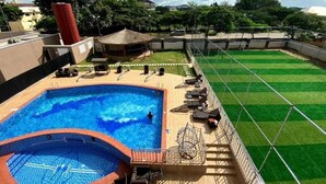 A rooftop swimming pool with a diving board, a sunshade, and a grassy area with lounge chairs. - JOEY HOMES  (Abuja)
