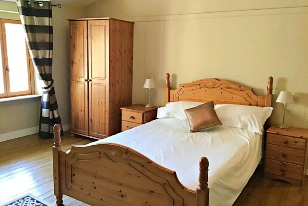 A bedroom with a wooden bed, two bedside tables, a wardrobe, and a window with curtains.