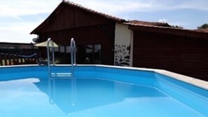 Une piscine avec un escalier en métal, un bâtiment en bois avec un toit en tuiles et un ciel dégagé.