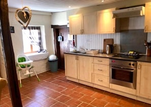 Une cuisine avec des meubles de rangement en bois clair, une cuisinière et une poubelle.
