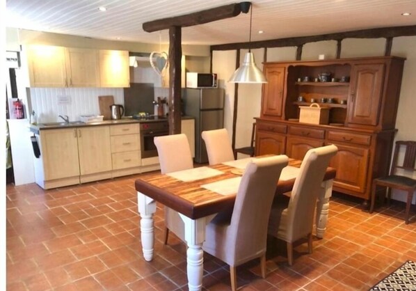 A kitchen with a wooden table and chairs, a hanging light fixture, and a wooden cabinet with shelves.