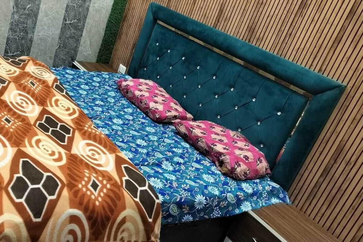 Een bed met een beddegoed met patroon en twee kussens, een gestapeld hoofdbord en een gestreept behang in de achtergrond.