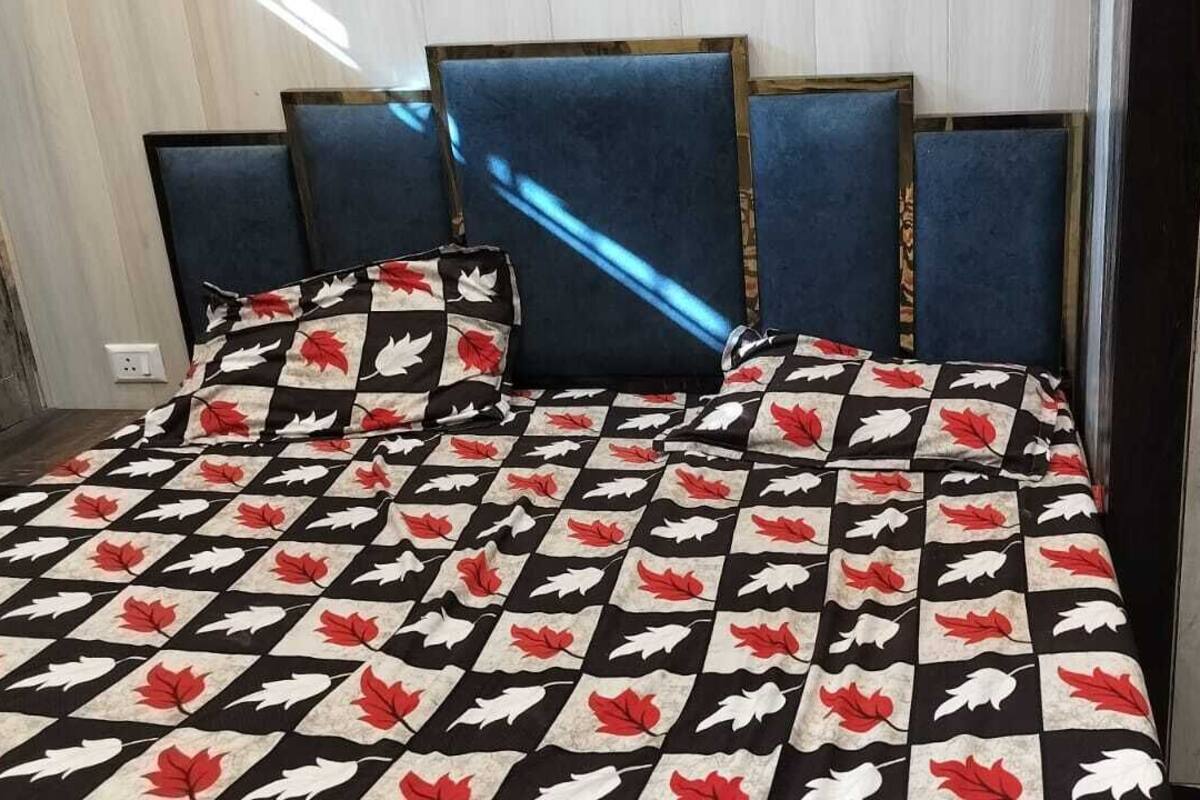 Een bed met een geruit sprei met rode en witte bladmotieven, omlijst door blauwe gestoffeerde hoofdeinden.