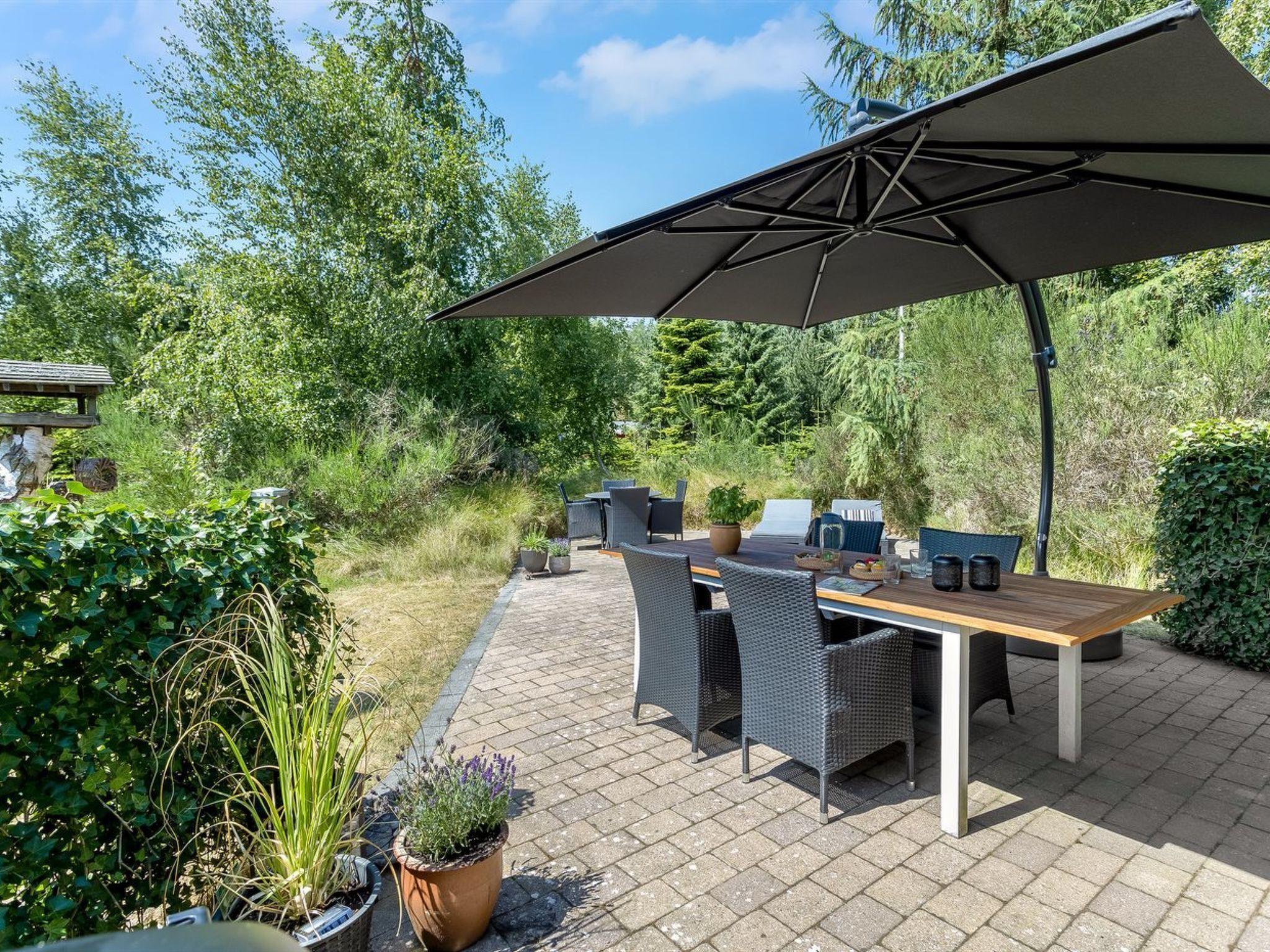 An outdoor patio with a wooden table and chairs, a large umbrella, and potted plants.