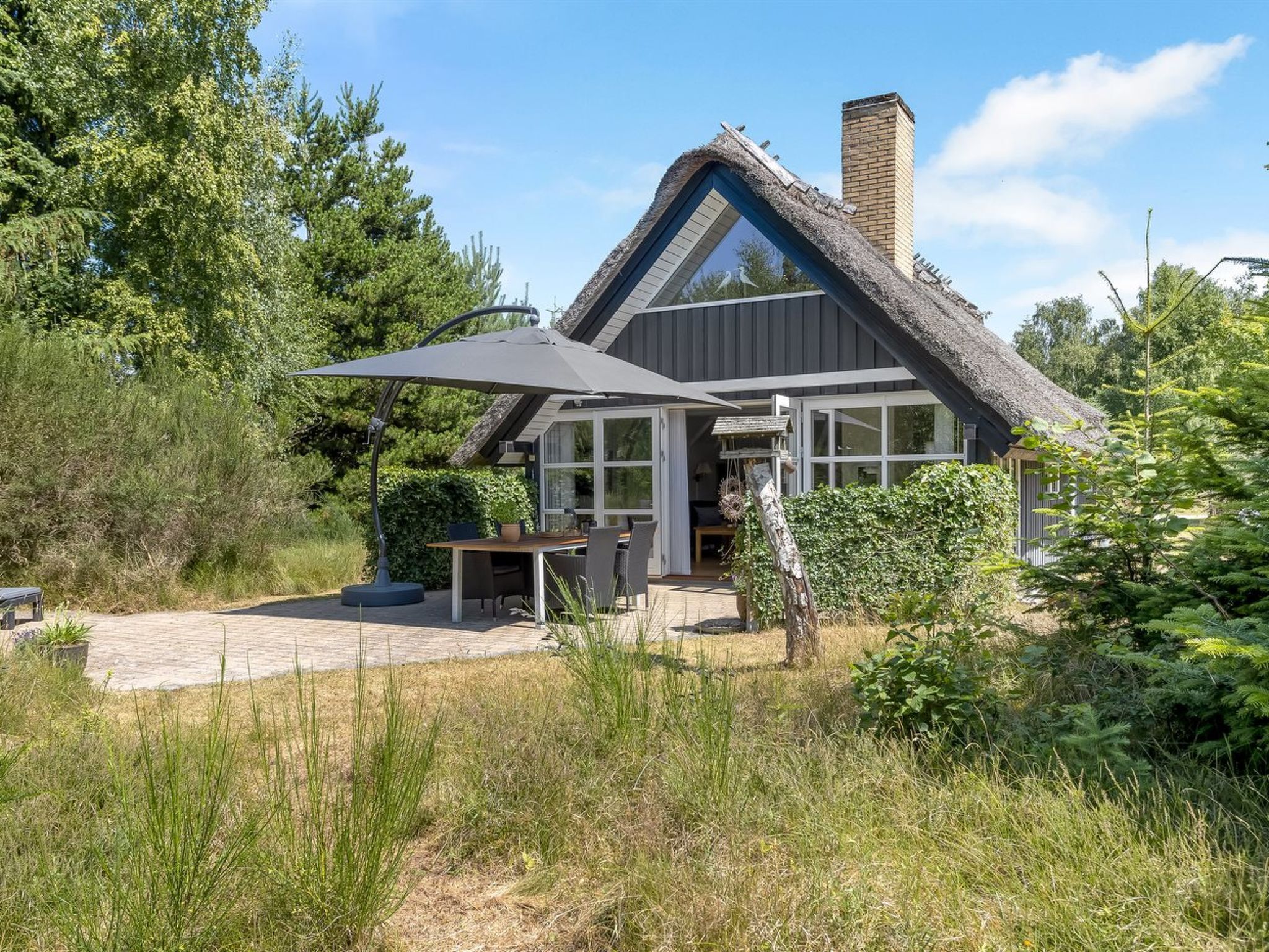 A modern house with a thatched roof, large windows, and a patio area with outdoor furniture.