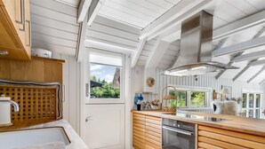 Une cuisine moderne avec des meubles en bois, une hotte de cuisine en acier inoxydable et une grande fenêtre offrant une vue sur la verdure environnante.