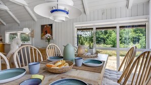 Un coin repas avec une table en bois dressée pour quatre personnes, entourée de chaises. Une grande fenêtre offre une vue sur la verdure à l’extérieur.