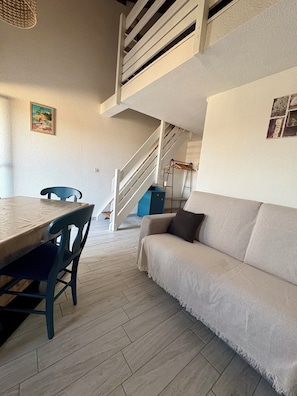 A modern living room with a dining table, a sofa, and a staircase leading to an upper level. - Iodine-filled getaway in St Palais sur mer - close to the beach - Apartment sleeps 4 (Saint-Palais-sur-Mer)