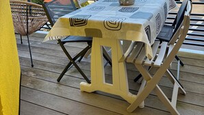 Un terrazzo in legno con tavolo e sedie, affacciato su una zona residenziale con case e alberi.