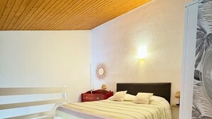 Una camera da letto con soffitto in legno, un letto con copriletto a righe, un comodino con una lampada e uno specchio fissato alla parete.