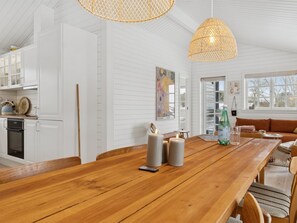 Una cocina amplia con armarios blancos, una mesa de comedor de madera e iluminación colgante.