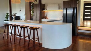 A modern kitchen with a central island, bar stools, a stainless steel refrigerator, and pendant lighting. - Surrounded by Nature With Panoramic Mountain Views (Lower Beechmont)