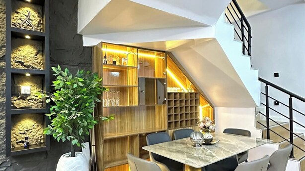 A modern dining area with a marble table and chairs, a potted plant, and a staircase leading to an upper level. - Yusuf Baba Shortlets (Abuja)