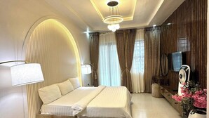 A modern bedroom with a large bed, a bedside table, a lamp, a TV, and a fan. - Yusuf Baba Shortlets (Abuja)