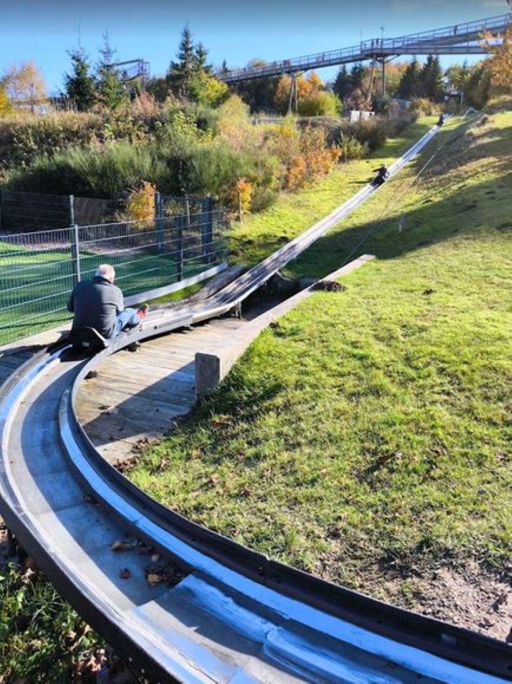 Eine gebogene Metallrutsche in einem Park, auf der Spitze sitzt eine Person.