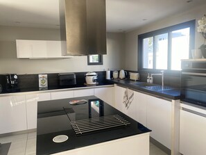 A modern kitchen with a black countertop, white cabinets, a built-in oven, and a window providing natural light. - Villa Evasion with swimming pool, close to the beach (Agde)