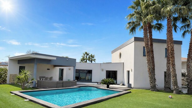 Une maison moderne dotée d’une piscine, de palmiers et d’une pelouse bien entretenue.