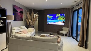 Un salon moderne avec un canapé, une table basse et un téléviseur à écran plat diffusant une image d’une plage tropicale.