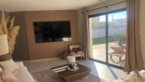 Un salon moderne doté d’un téléviseur à écran plat, d’un canapé, d’une table basse et d’une porte-fenêtre coulissante donnant sur une terrasse extérieure.