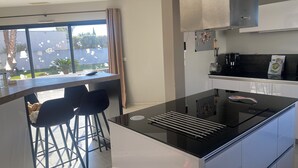 Une cuisine moderne dotée d’un îlot central, de tabourets de bar, d’une cuisinière intégrée et offrant une vue sur l’extérieur.