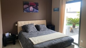 Une chambre à coucher avec un grand lit, une table de chevet, une œuvre d’art accrochée au mur et une vue sur l’extérieur.