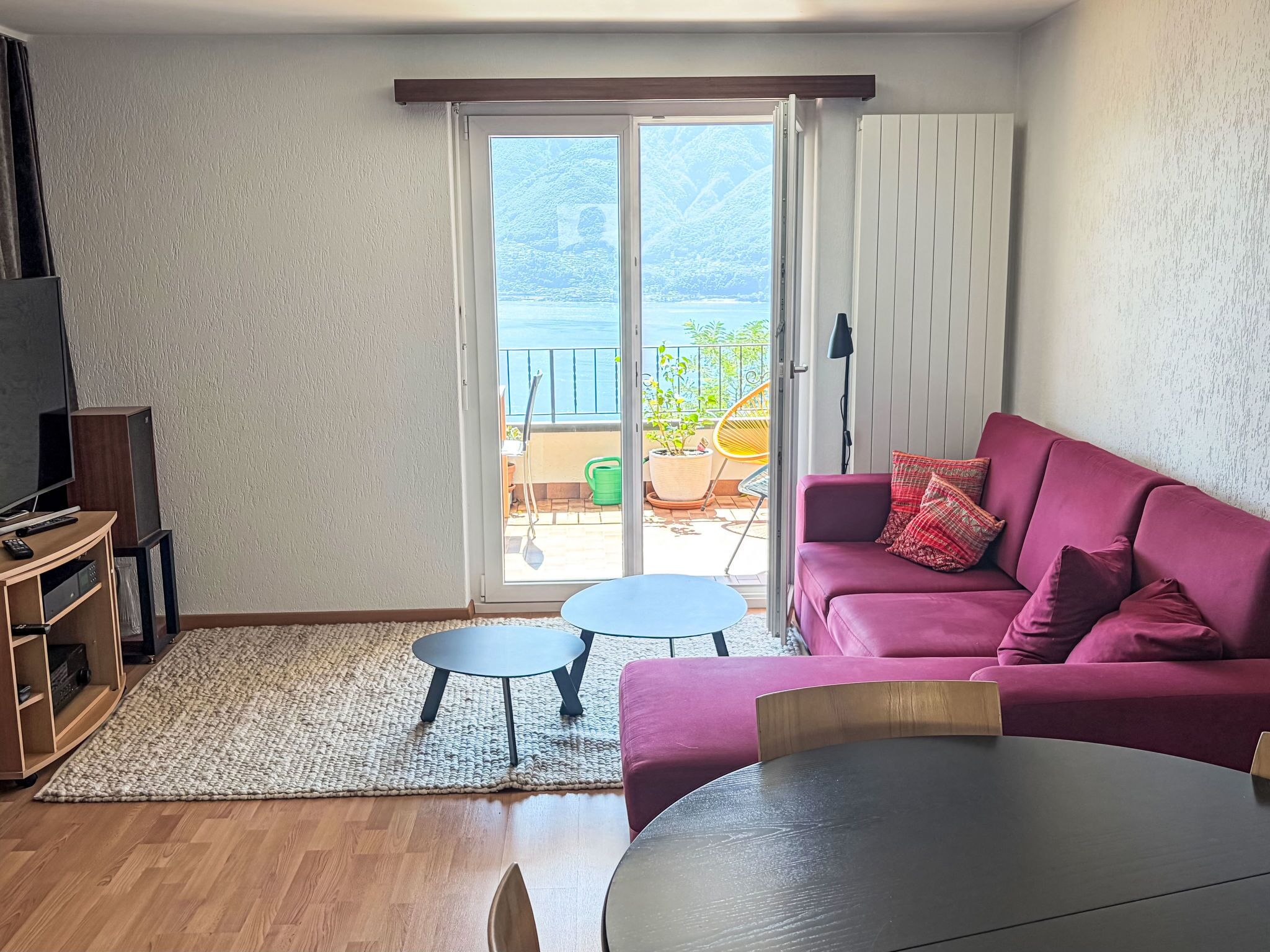 Ein Wohnzimmer mit einem rosafarbenen Sofa, einem Fernseher und einer Glastür, die auf einen Balkon führt.