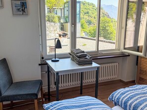 A room with a bed, a desk, and a chair. There is a window with a view of trees and mountains. - Casa Giovanna Ronco sopra Ascona by Interhome (Ronco sopra Ascona)