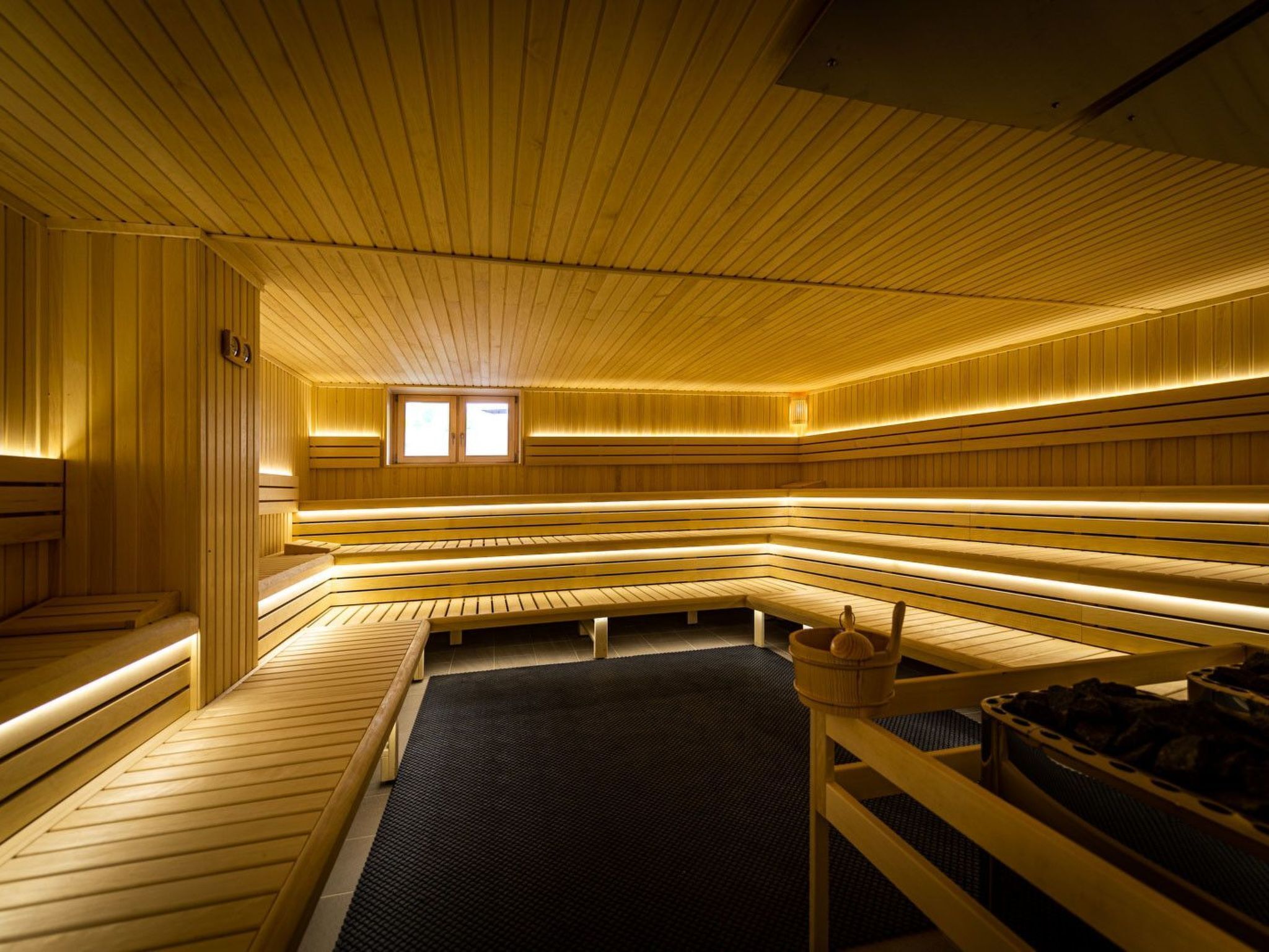 Un sauna doté de bancs en bois et d’un plancher chauffé, éclairé par un éclairage chaleureux.
