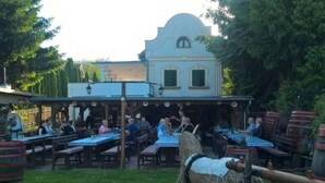 Un espacio de comedor al aire libre con mesas y sillas, un edificio de fachada azul y una escultura de paja en primer plano.