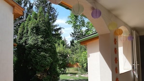 A covered outdoor area with a paved walkway, surrounded by greenery and trees.