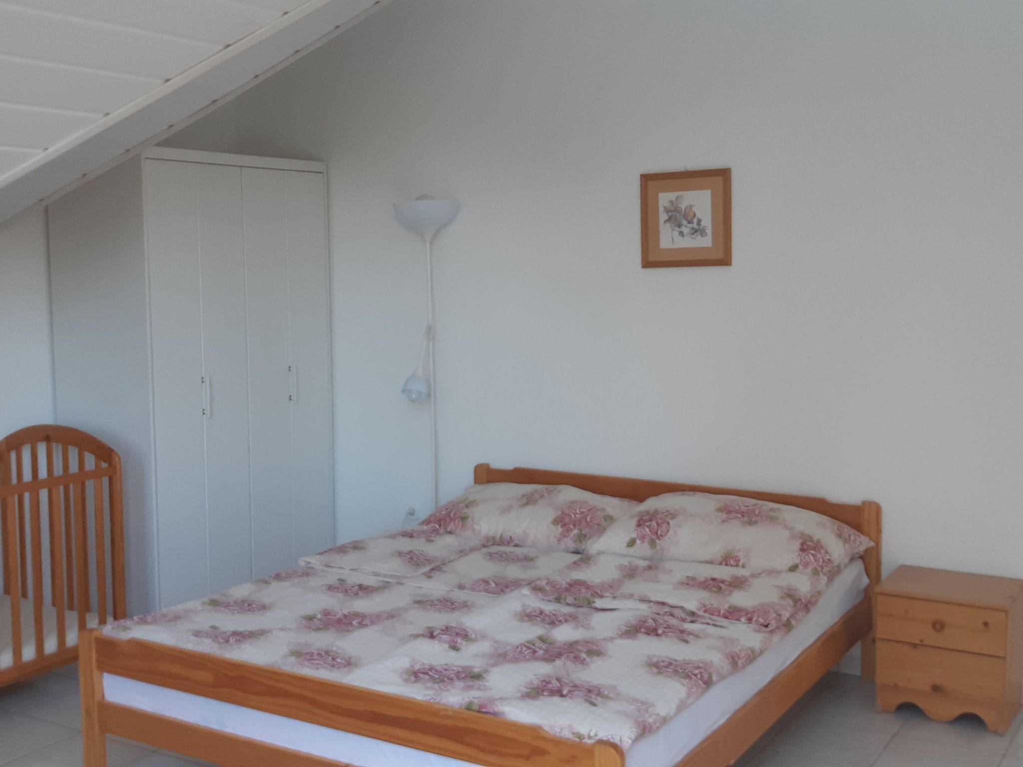 Un dormitorio con cama de madera, una mesita de noche, una cuna, un armario y una lámpara de pared.